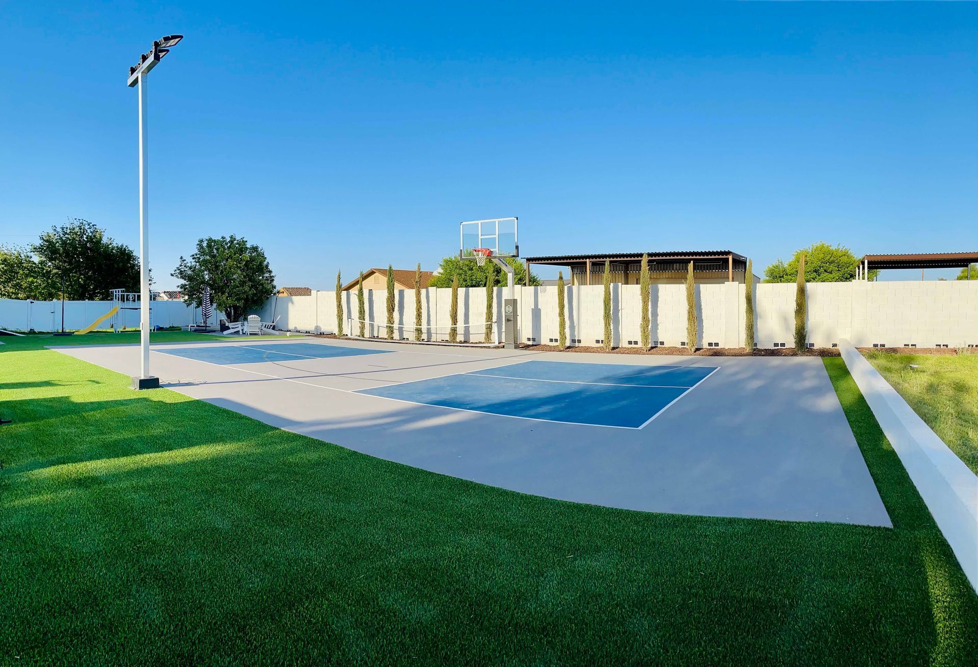 There is a basketball court in the middle of a grassy field.