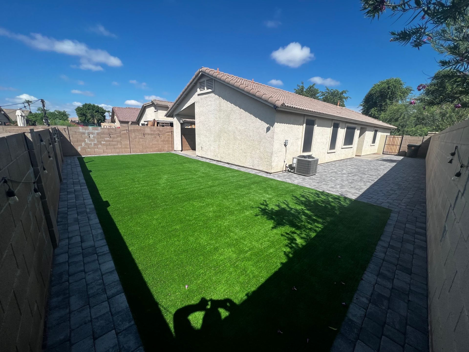 A shadow of a person is cast on the grass in front of a house.
