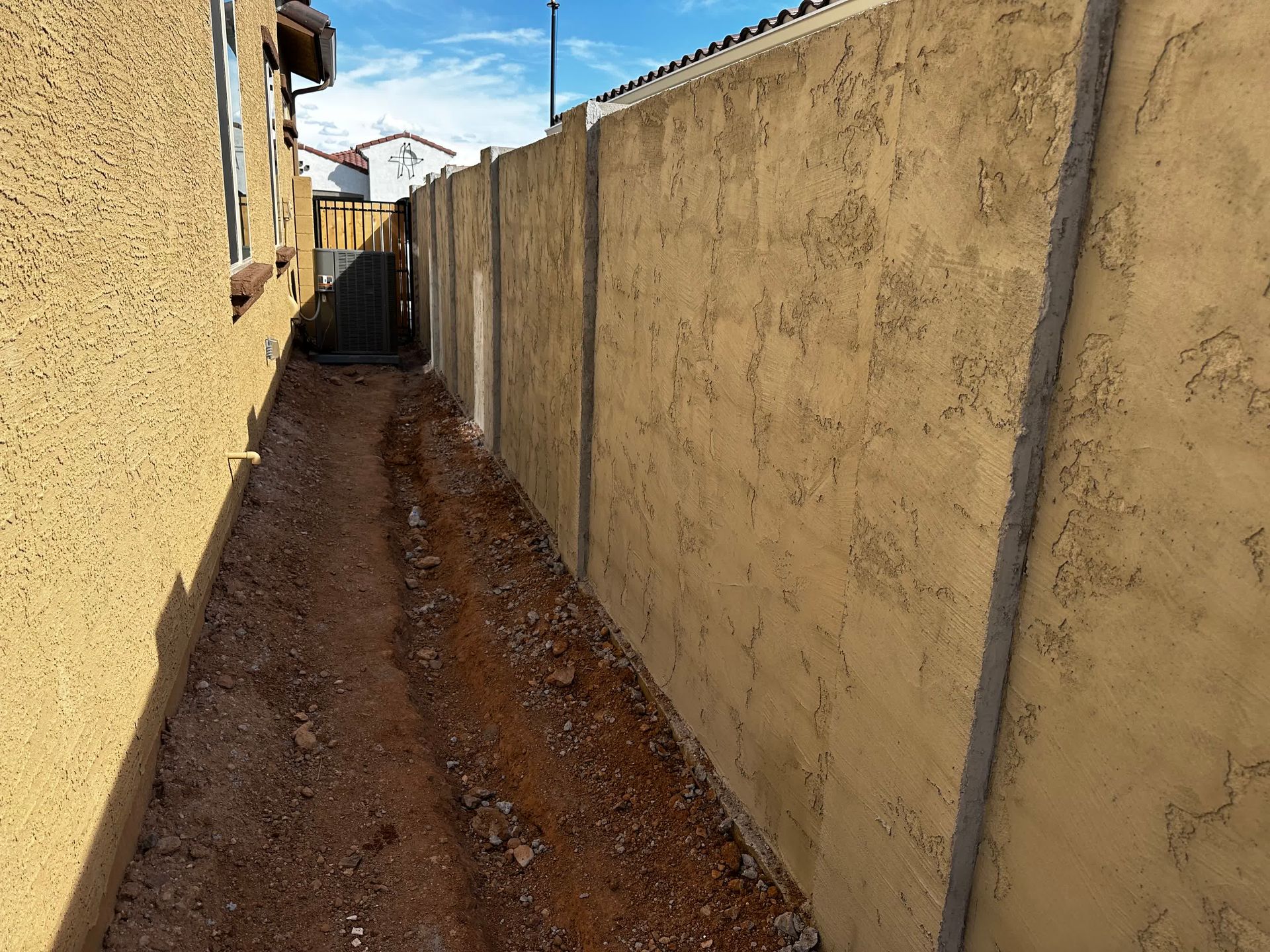A narrow path between two buildings with a fence in the background