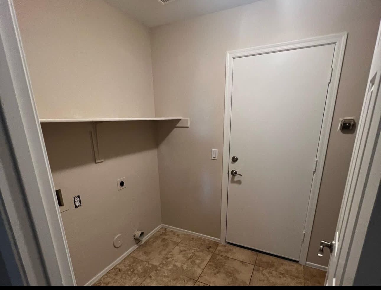 A laundry room with a door and a shelf on the wall.