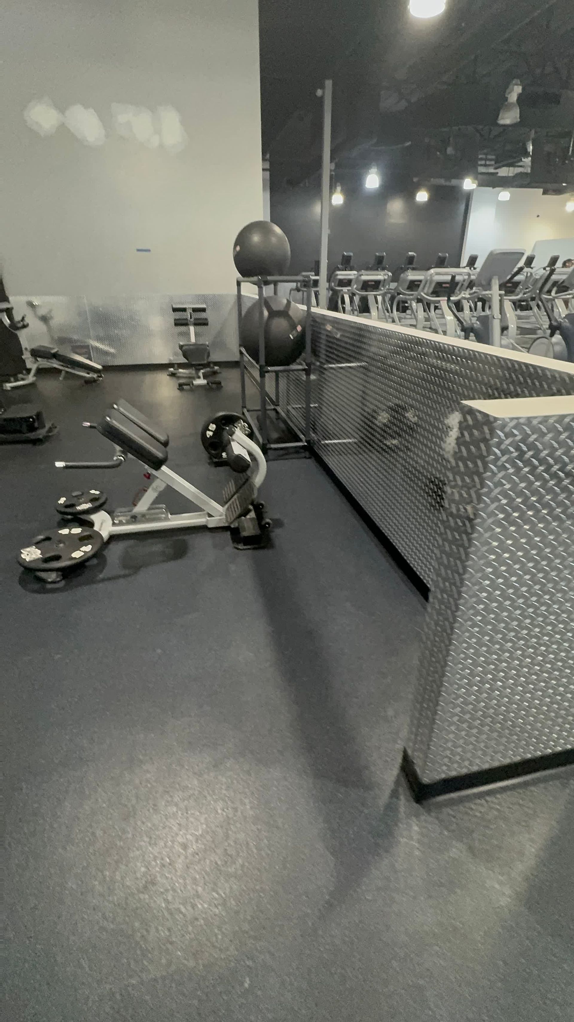 A black and white photo of a gym with a bench and dumbbells.