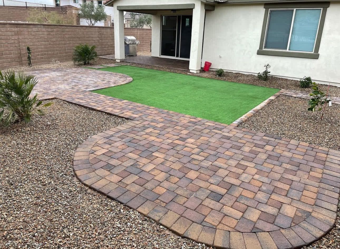 A brick walkway leading to a house with a green lawn in the backyard.