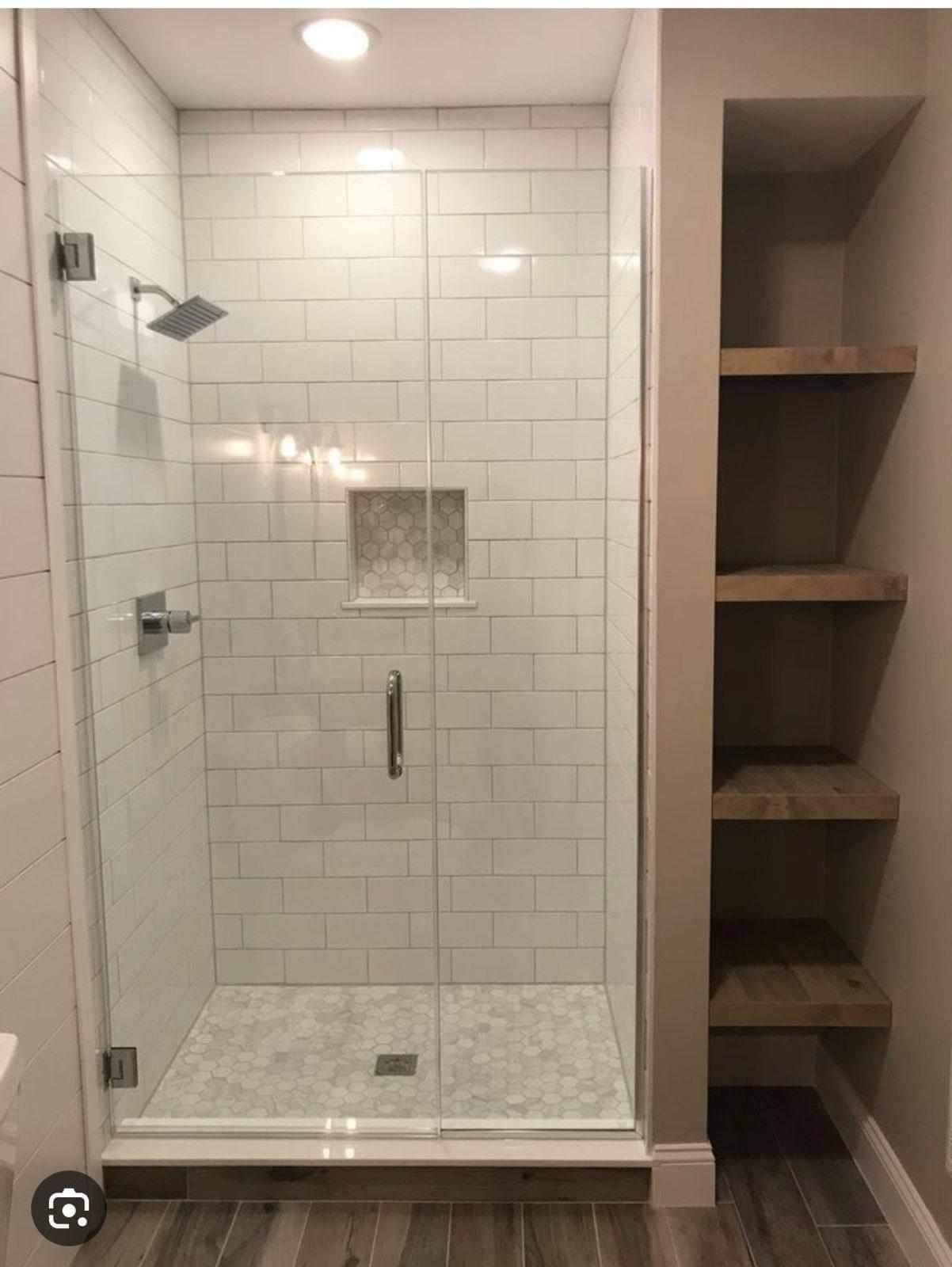 A bathroom with a walk in shower with a glass door and shelves.