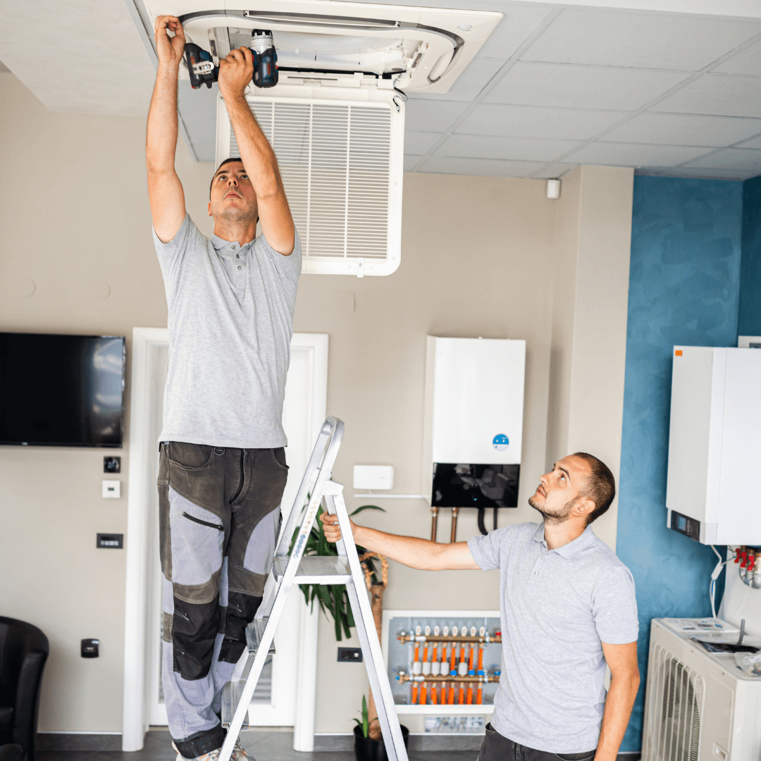 Two men are working on an air conditioner in a living room.