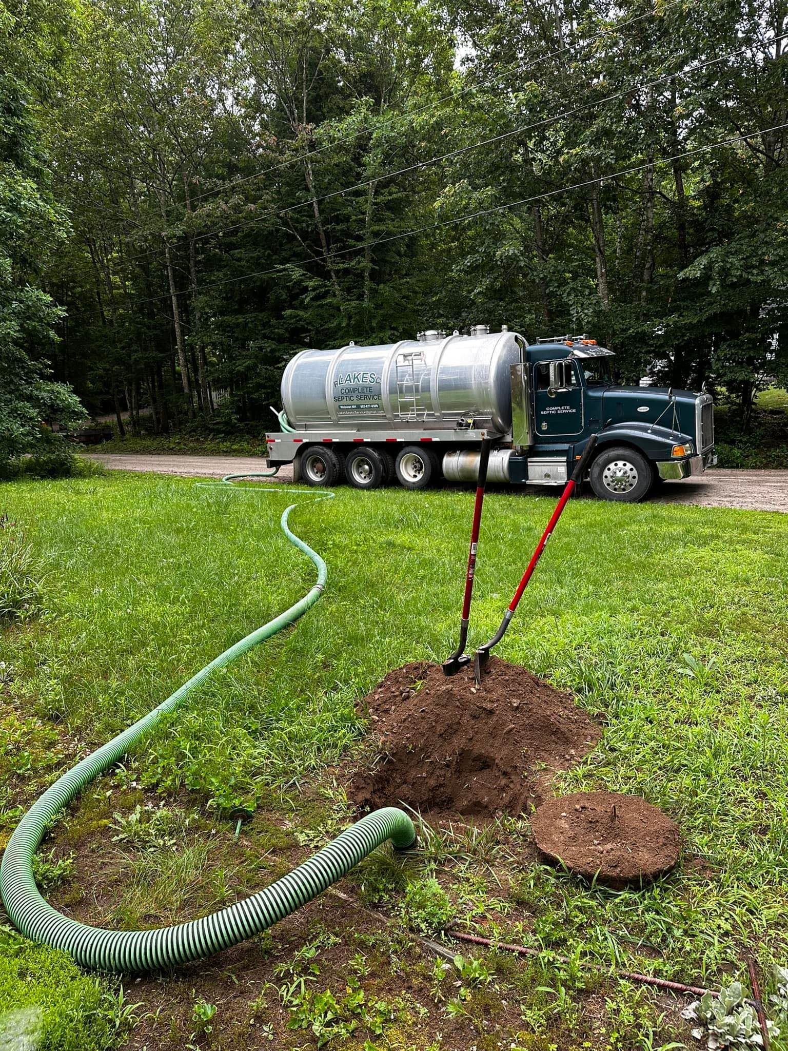 Septic truck parked on grass, hose in ground near open tank access.