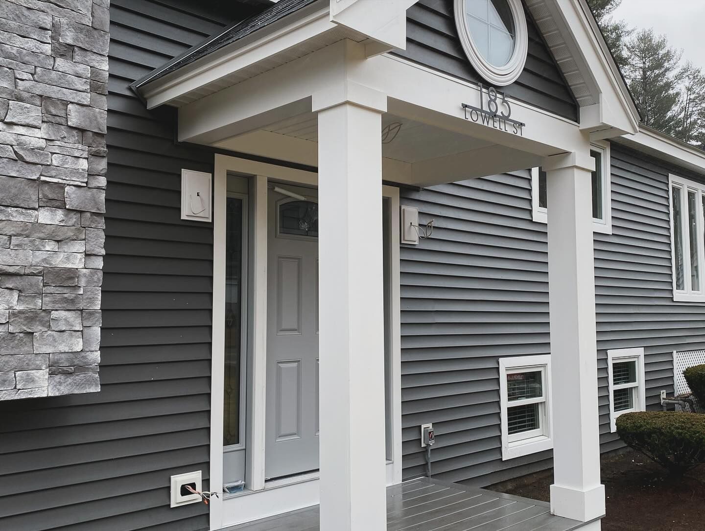 A gray house with a white porch and a clock on the front of it.