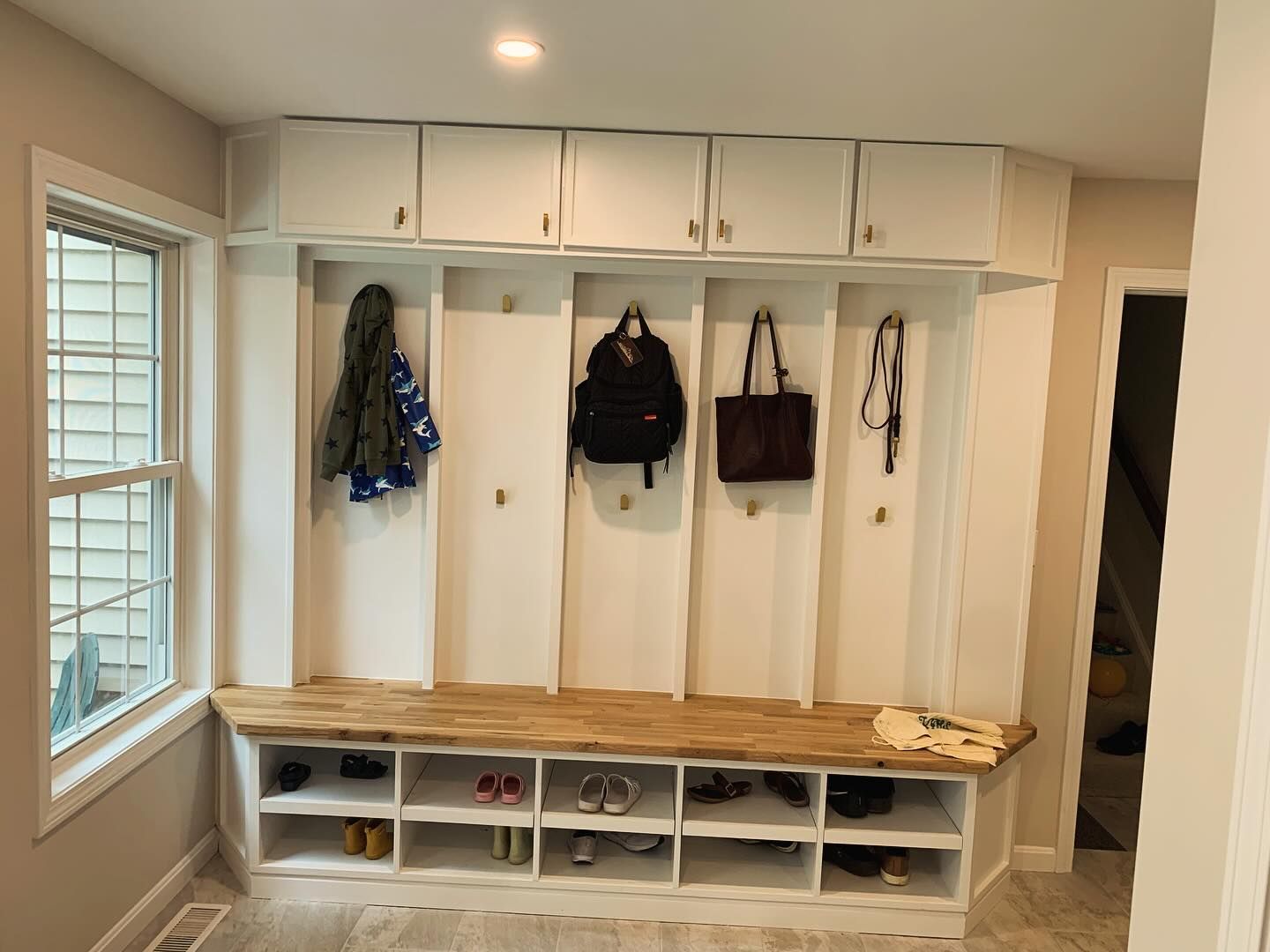 A room with a bench , shelves , hooks and a window.