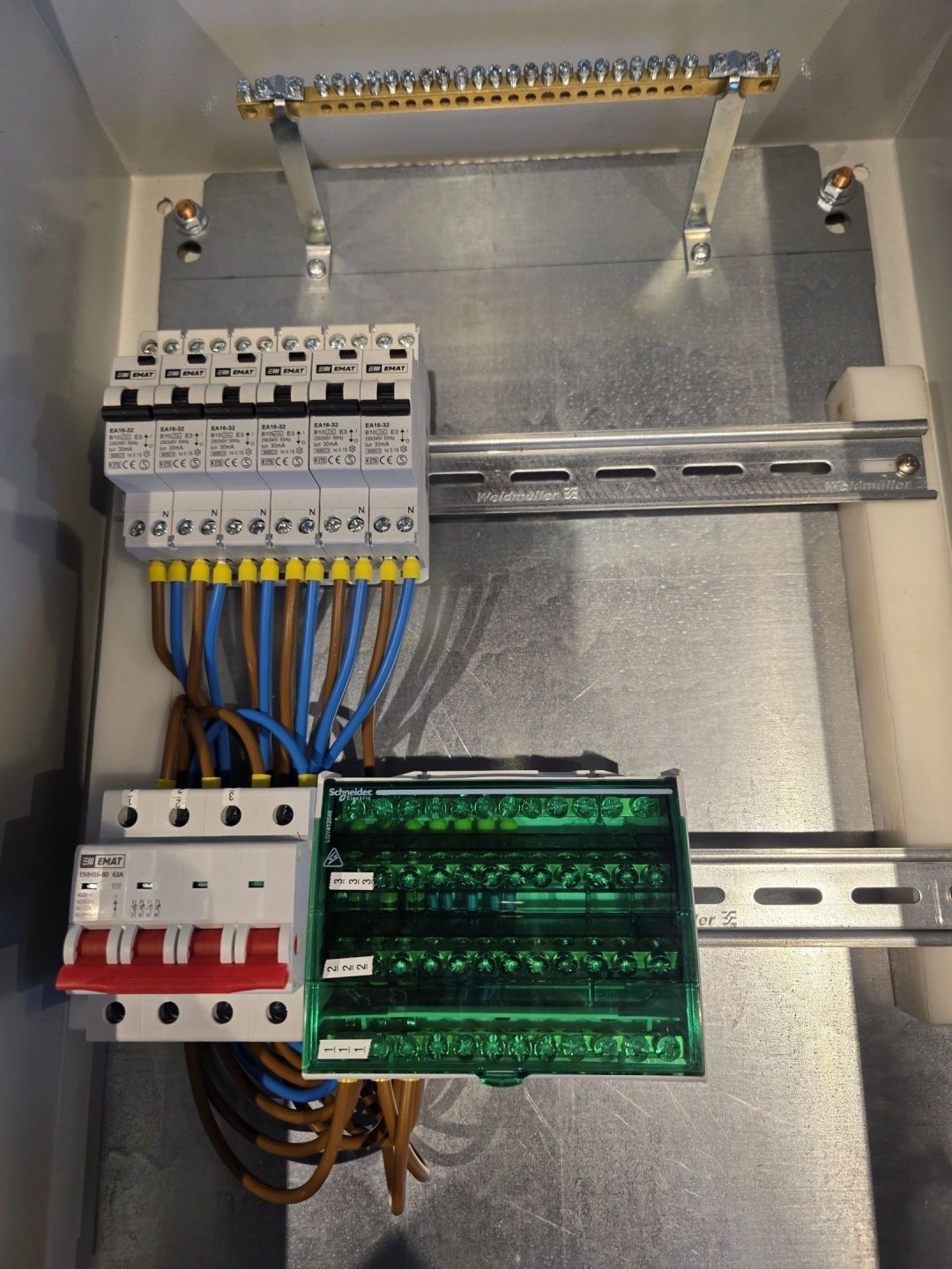 Elektrisch schakelpaneel met stroomonderbrekers en groene klemmenblokken, gemonteerd op DIN-rails.