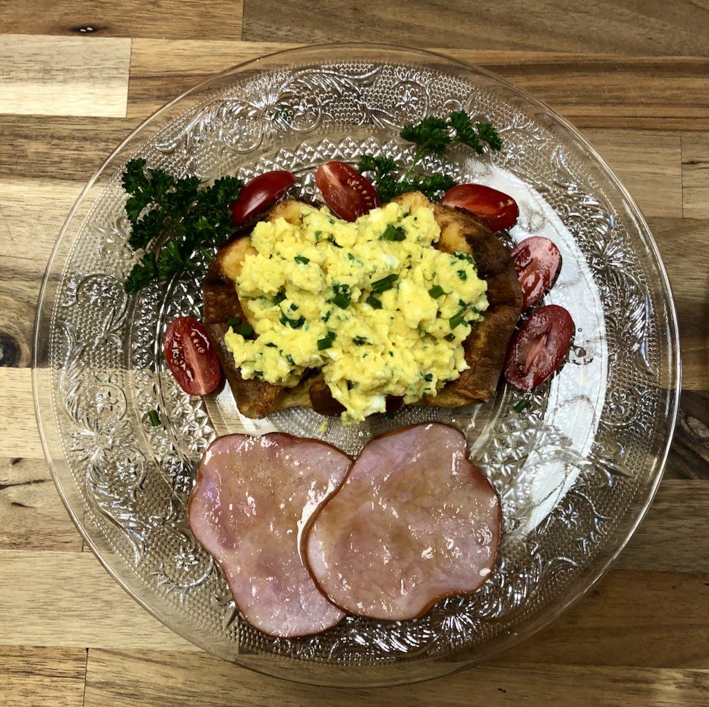 A plate of food with scrambled eggs ham and tomatoes on a wooden table.