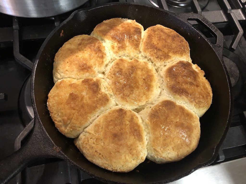 A skillet filled with biscuits is sitting on a stove.