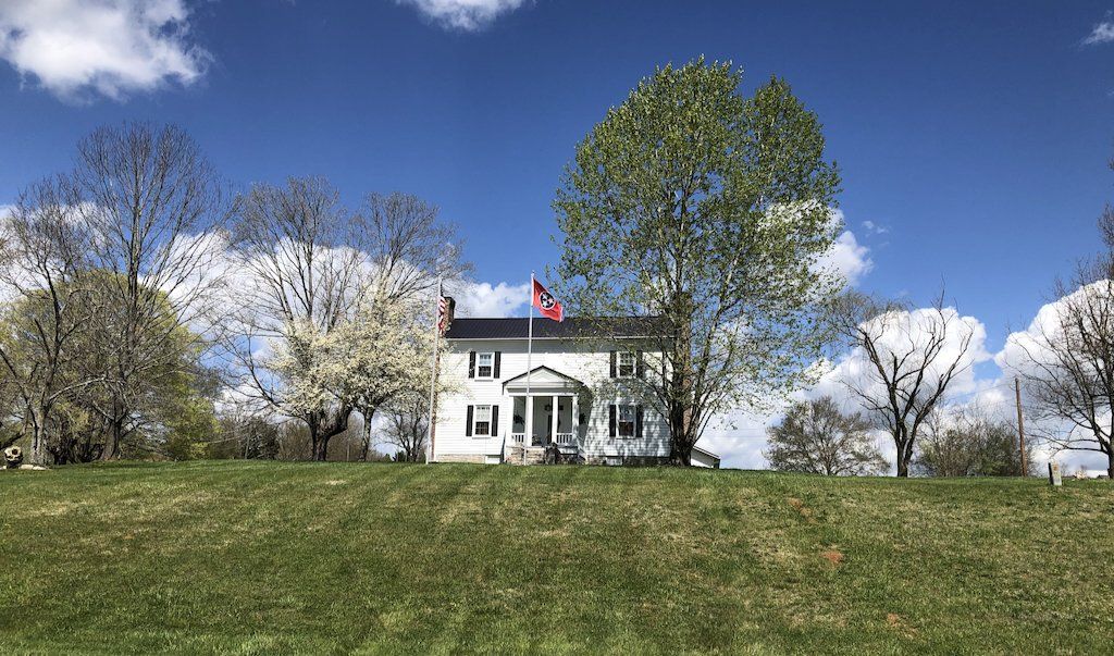 A white house is sitting on top of a grassy hill surrounded by trees.