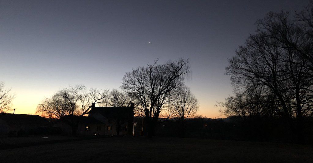 A sunset with a house and trees in the foreground