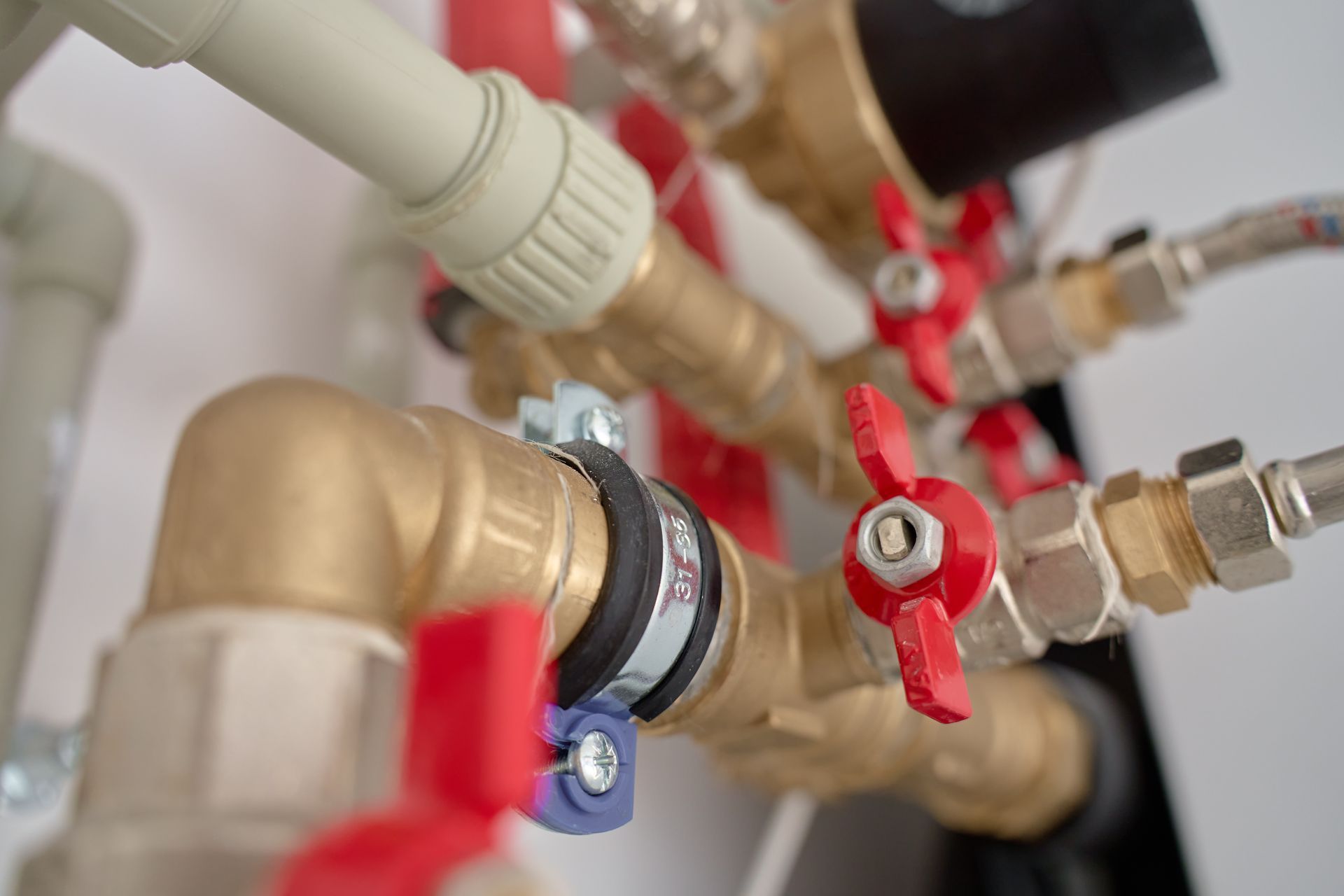 Close-up of brass plumbing pipes and red shutoff valves with fittings in a mechanical room Close-up of brass plumbing pipes and red shutoff valves with fittings in a mechanical room
