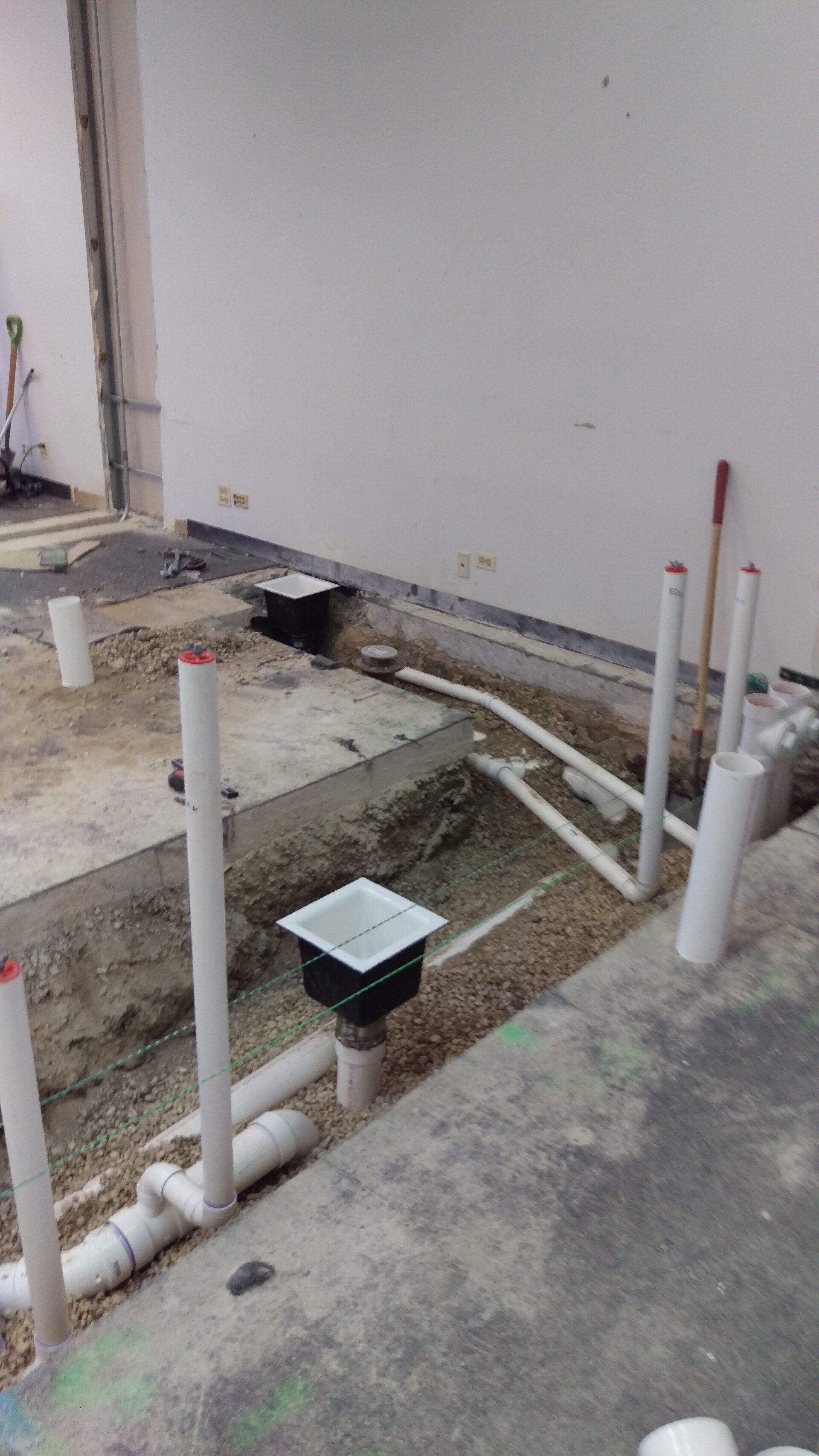 Construction site with white PVC pipes and drains in a concrete floor.