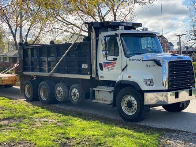 White dump truck parked on the side of a road, with a full bed, in front of a residential area.