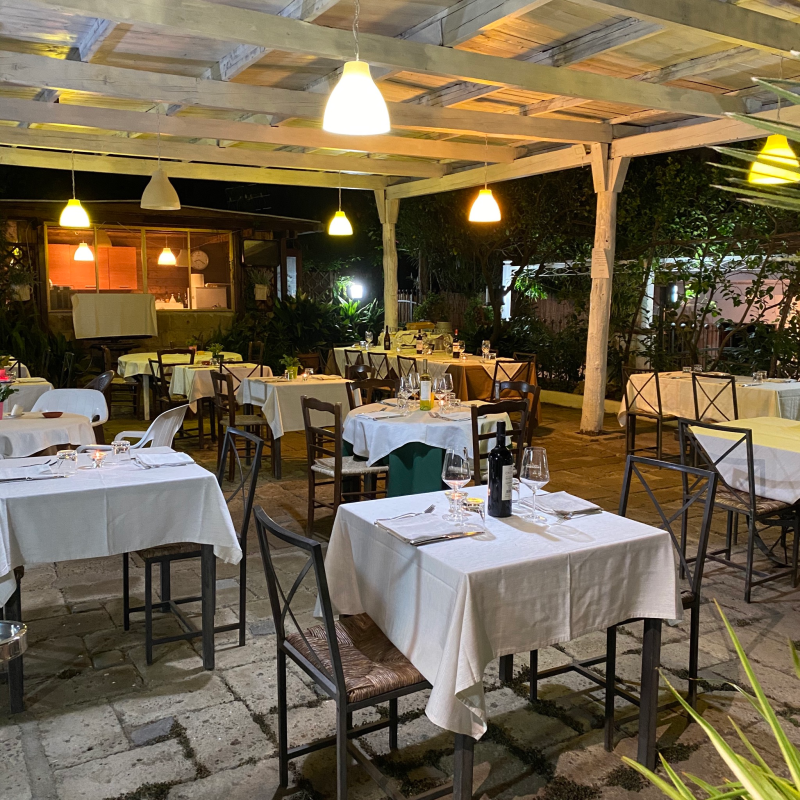 Patio esterno del ristorante con tovaglie bianche, luci sospese e sedie.