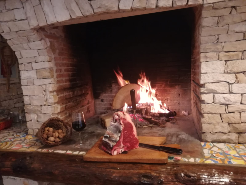 Bistecca e vino rosso disposti su un tagliere di legno davanti a un camino scoppiettante.