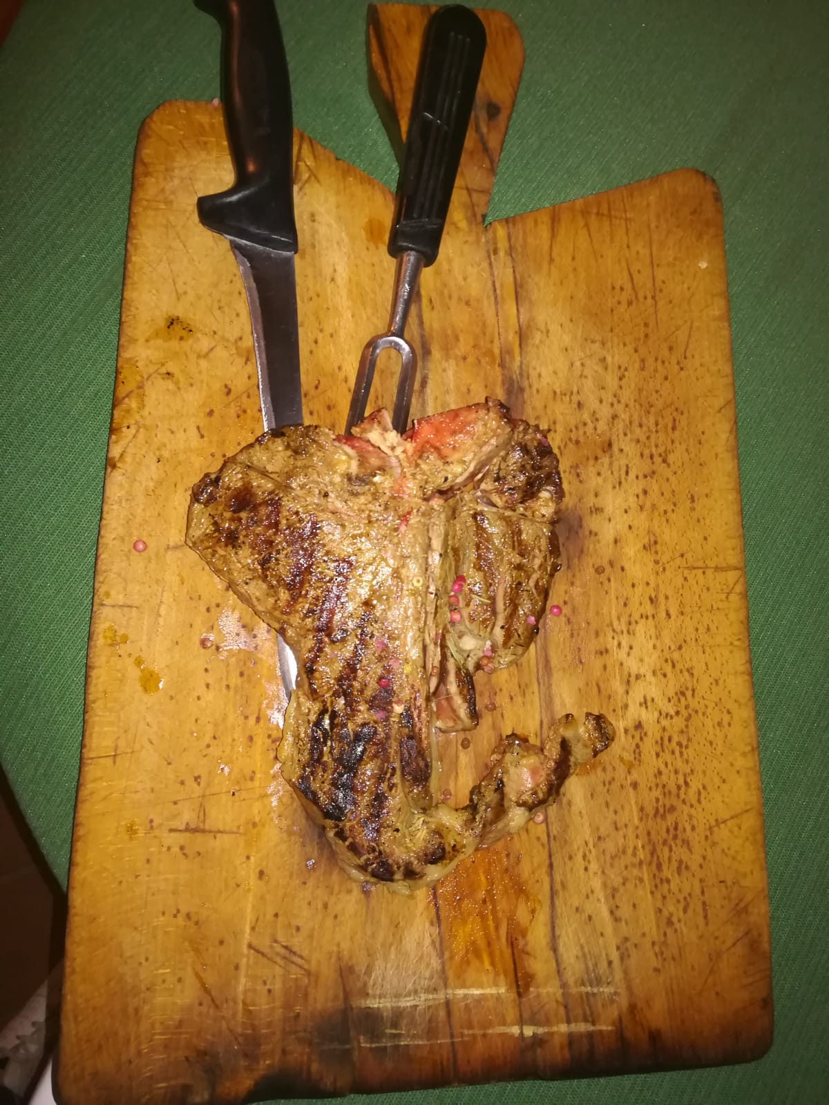Bistecca alla griglia su un tagliere di legno con coltello e forchetta.