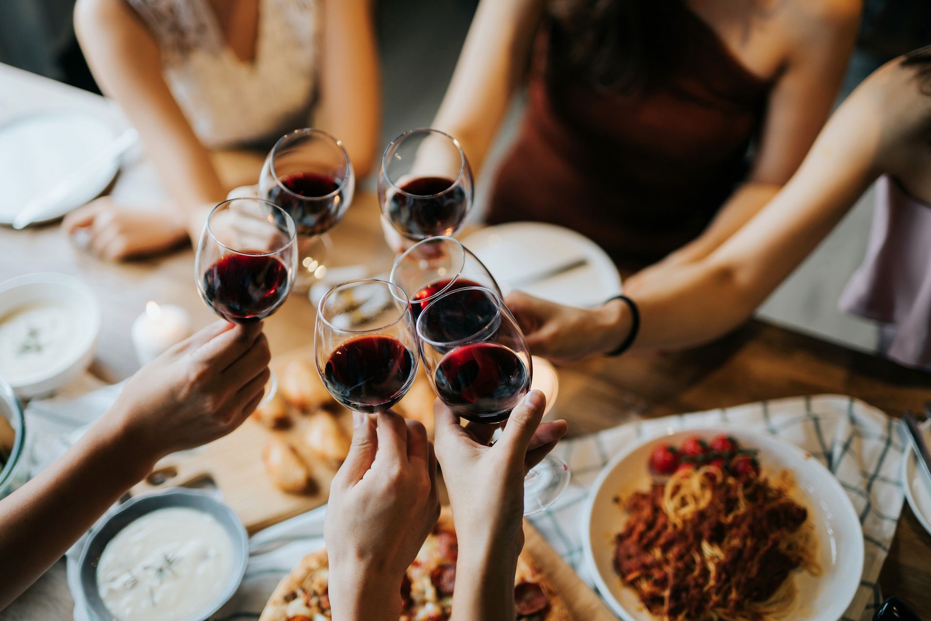 Persone che brindano con bicchieri di vino rosso a tavola con del cibo.