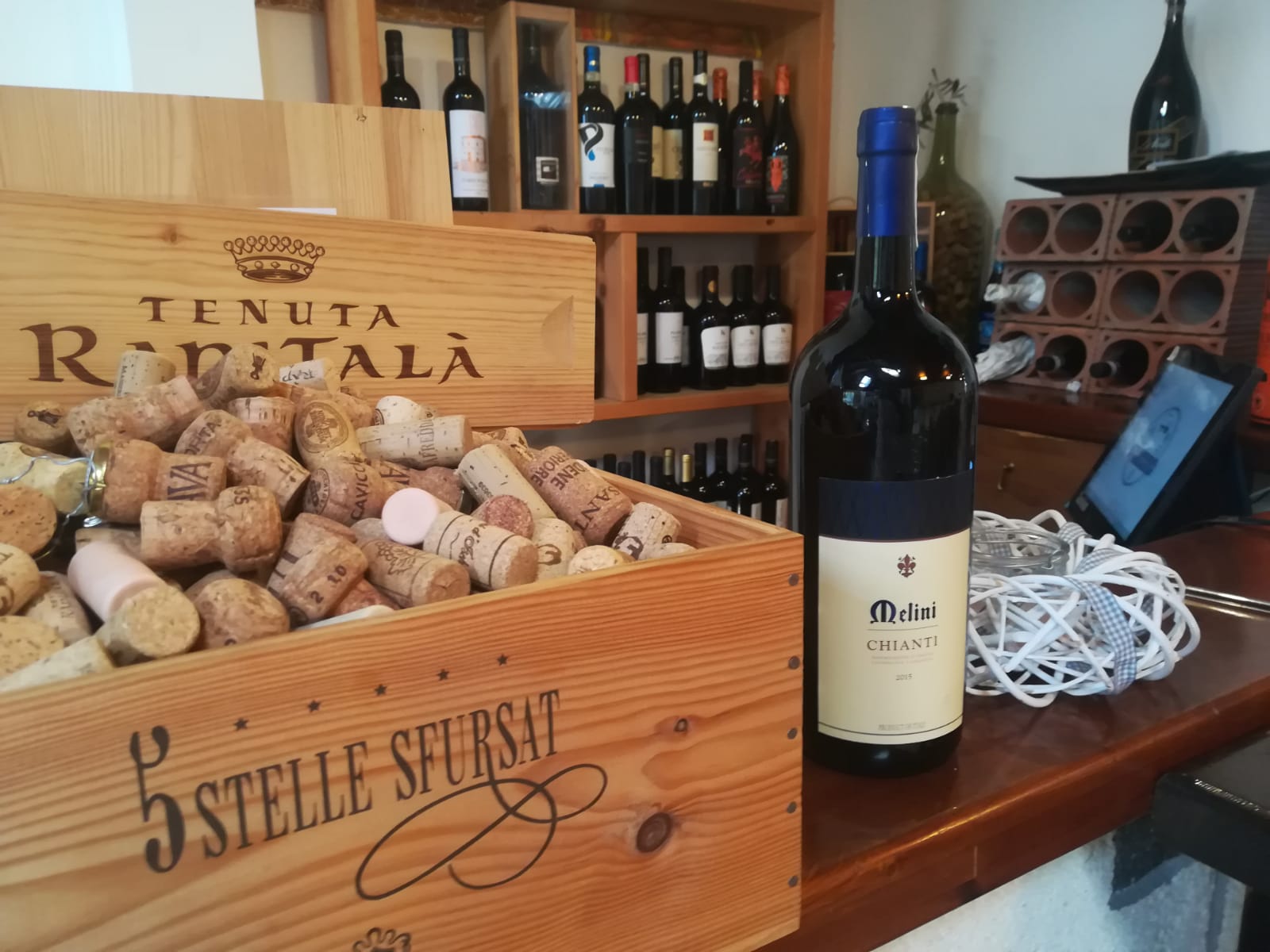 Una cassa di legno piena di tappi di sughero accanto a una bottiglia di vino rosso su un bancone.