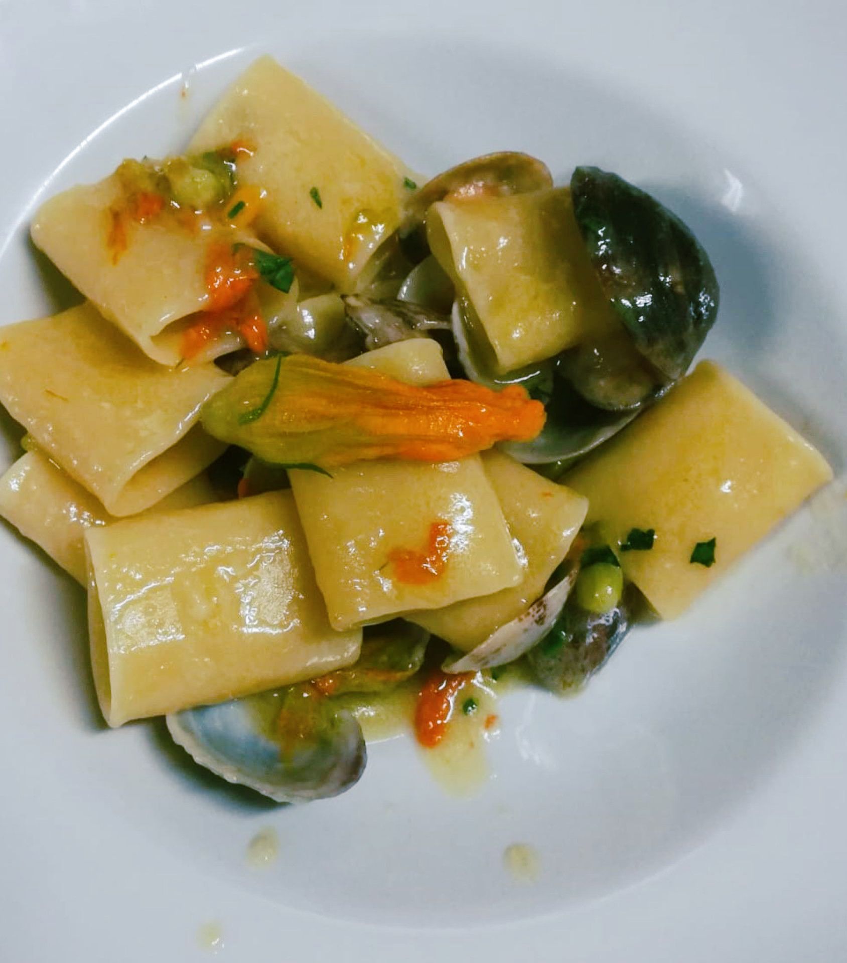 Pasta con vongole e fiori di zucca in una ciotola bianca.