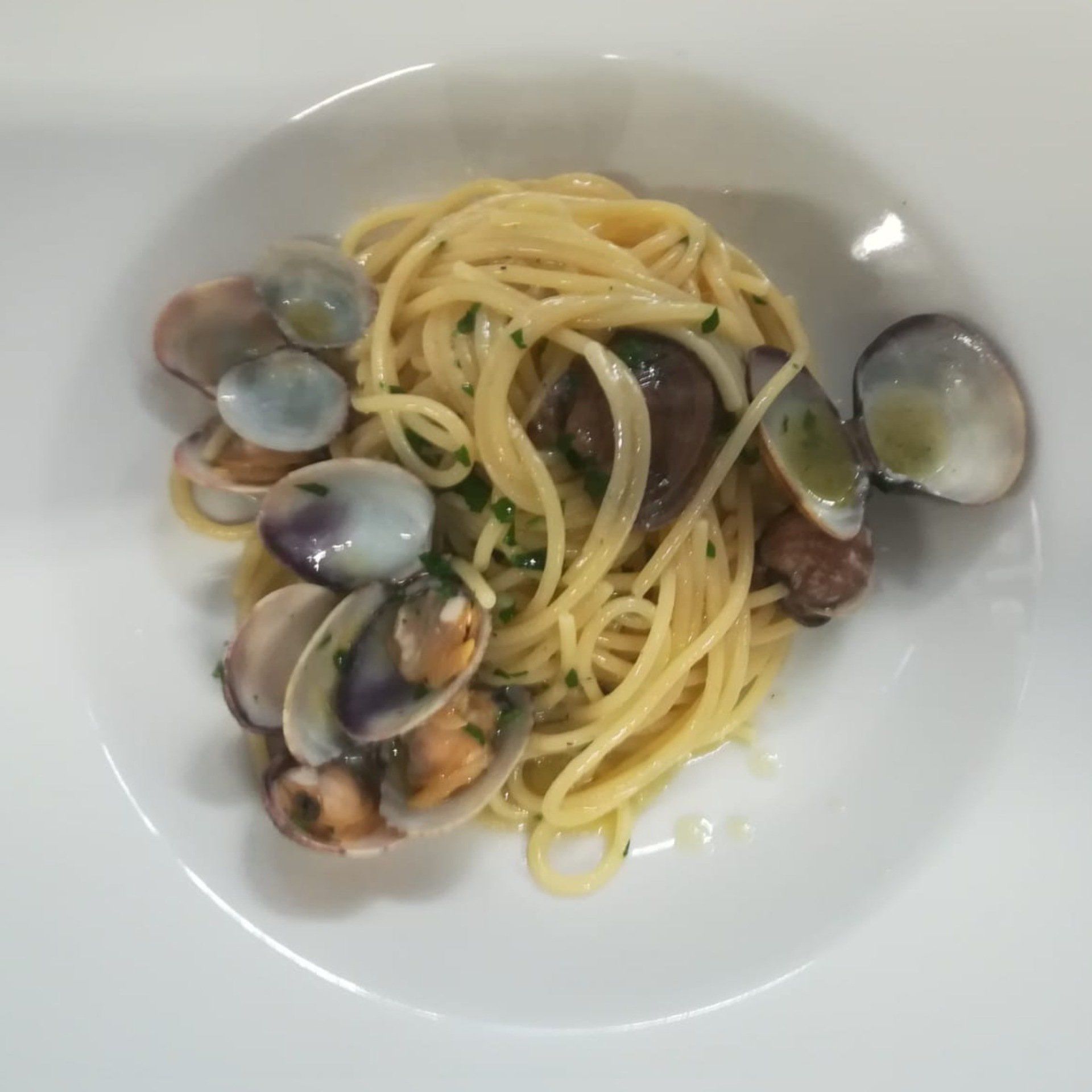 Spaghetti alle vongole in una ciotola bianca. Le vongole sono aperte, alcune con il guscio visibile.