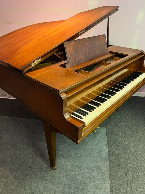 A black grand piano with a matching bench sits on a wooden stage in front of white columns and dark red curtains.