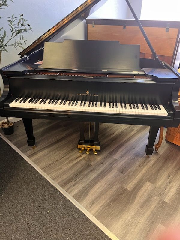 A black grand piano with a matching bench placed by a large bay window in a room with hardwood floors.