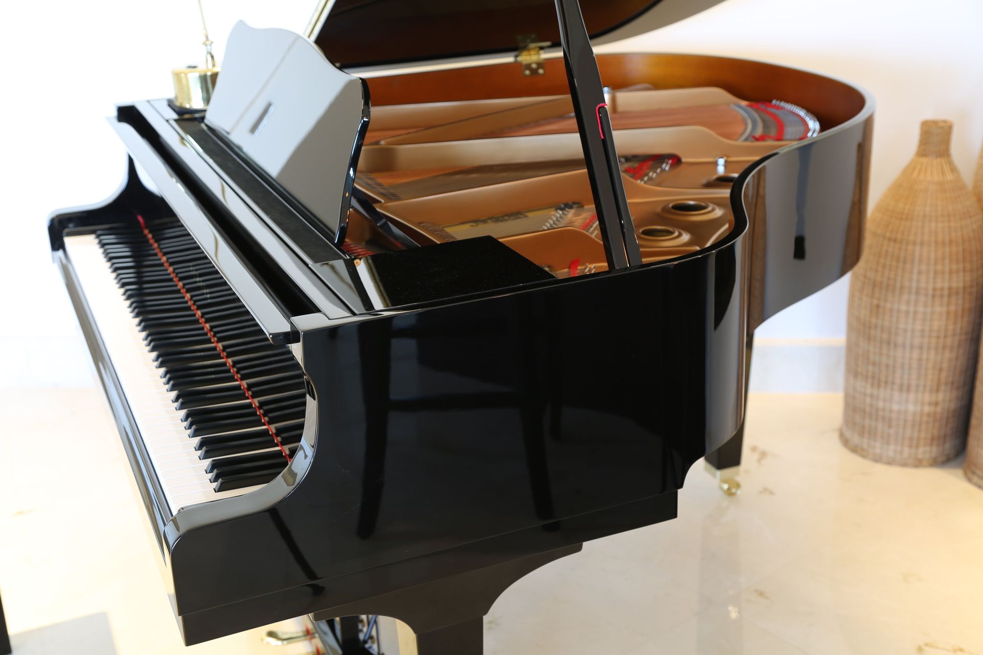 A glossy black grand piano with an open lid, positioned in a bright room next to textured wicker floor vases.
