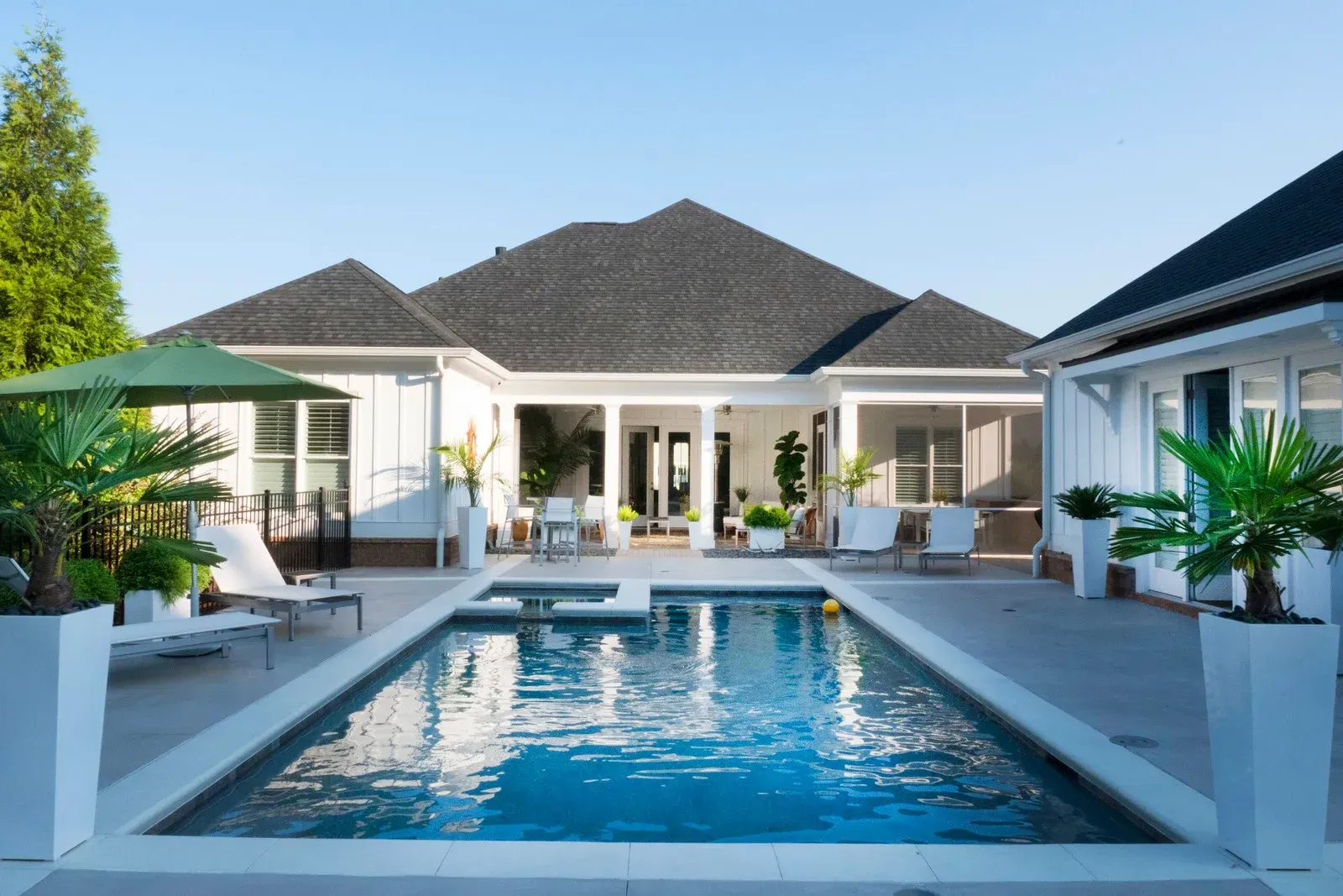 A luxury backyard with a rectangular pool, white house, and lounge chairs.