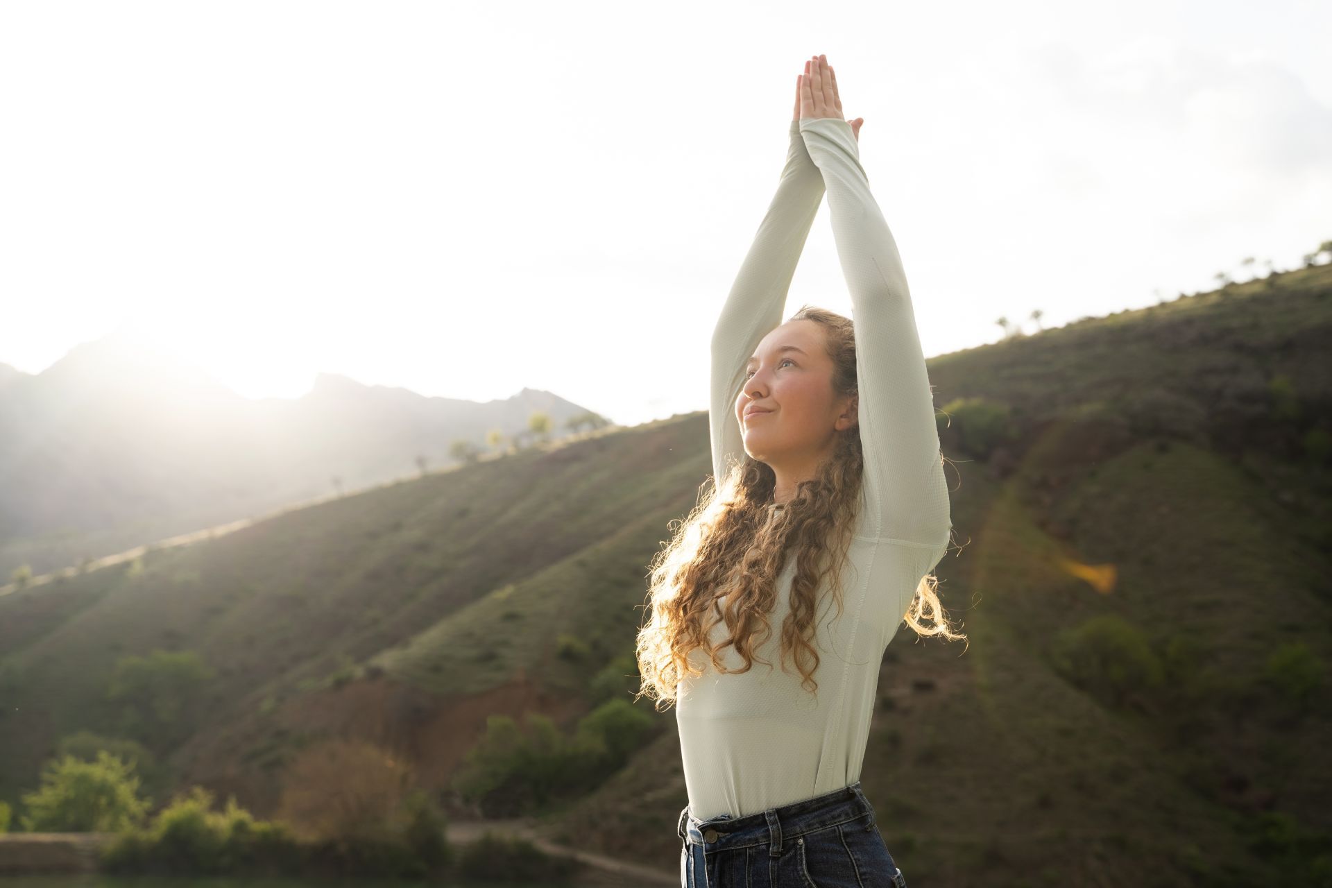 Person standing outdoors with arms raised in a sunlit mountain valley