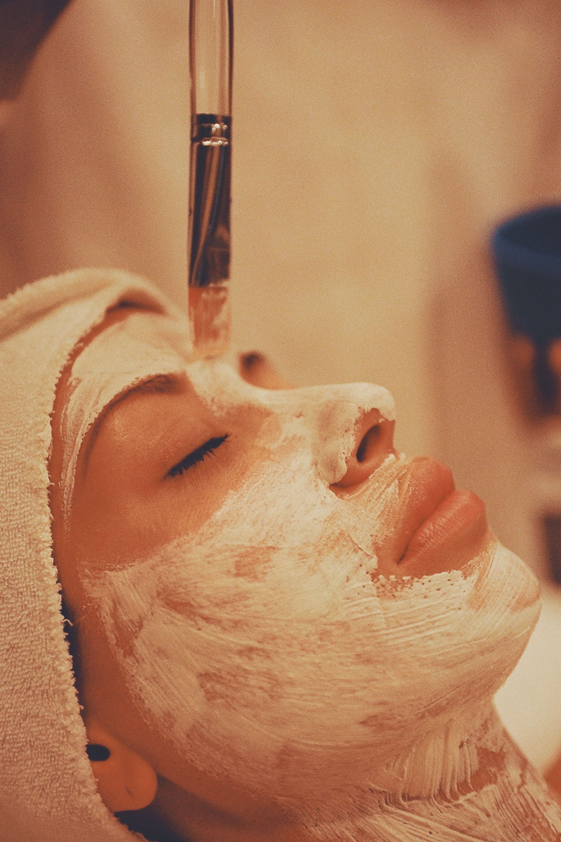 Person receiving a white facial mask with a brush during a spa treatment