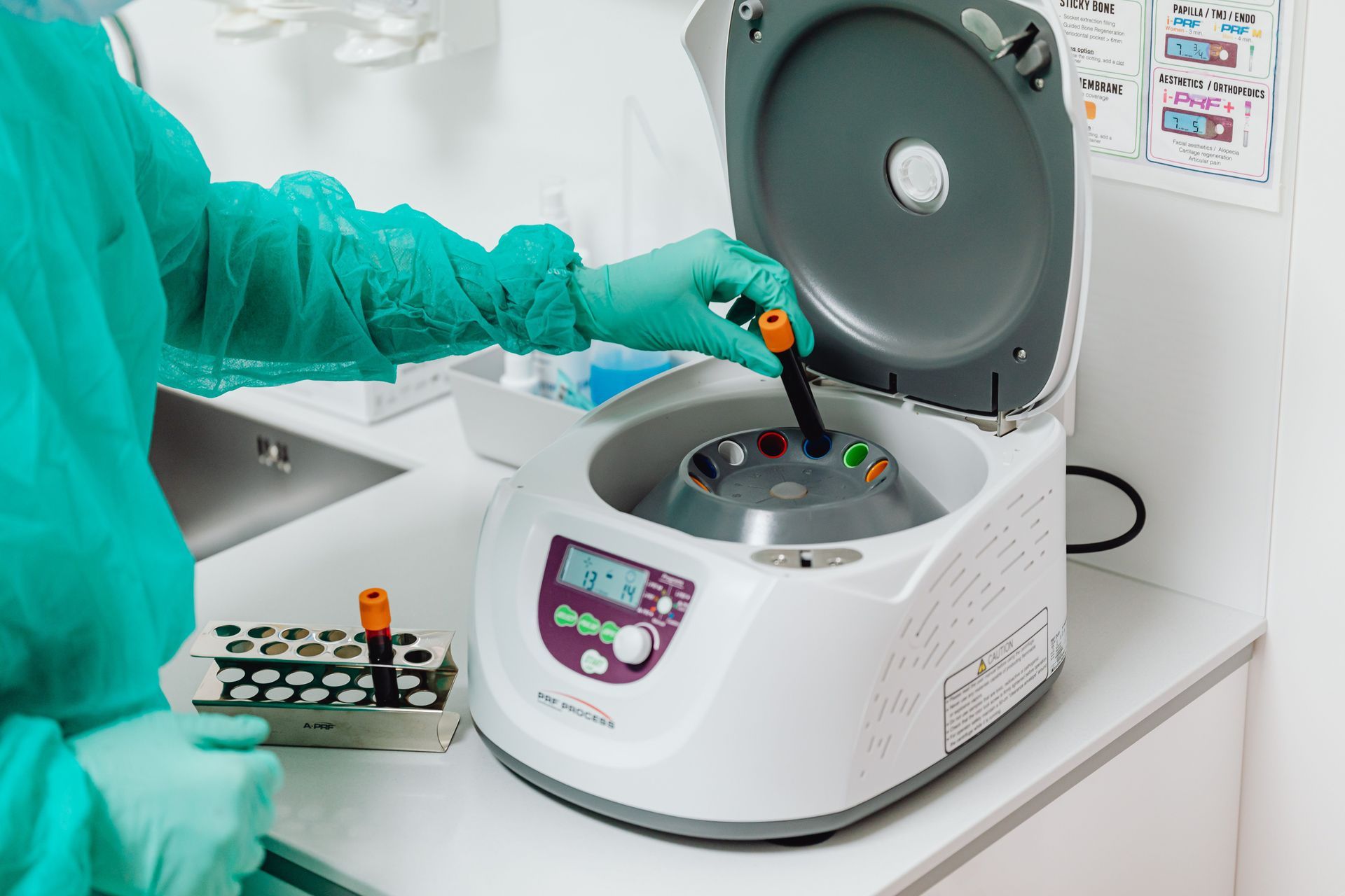 Gloved technician loading test tubes into a lab centrifuge on a countertop