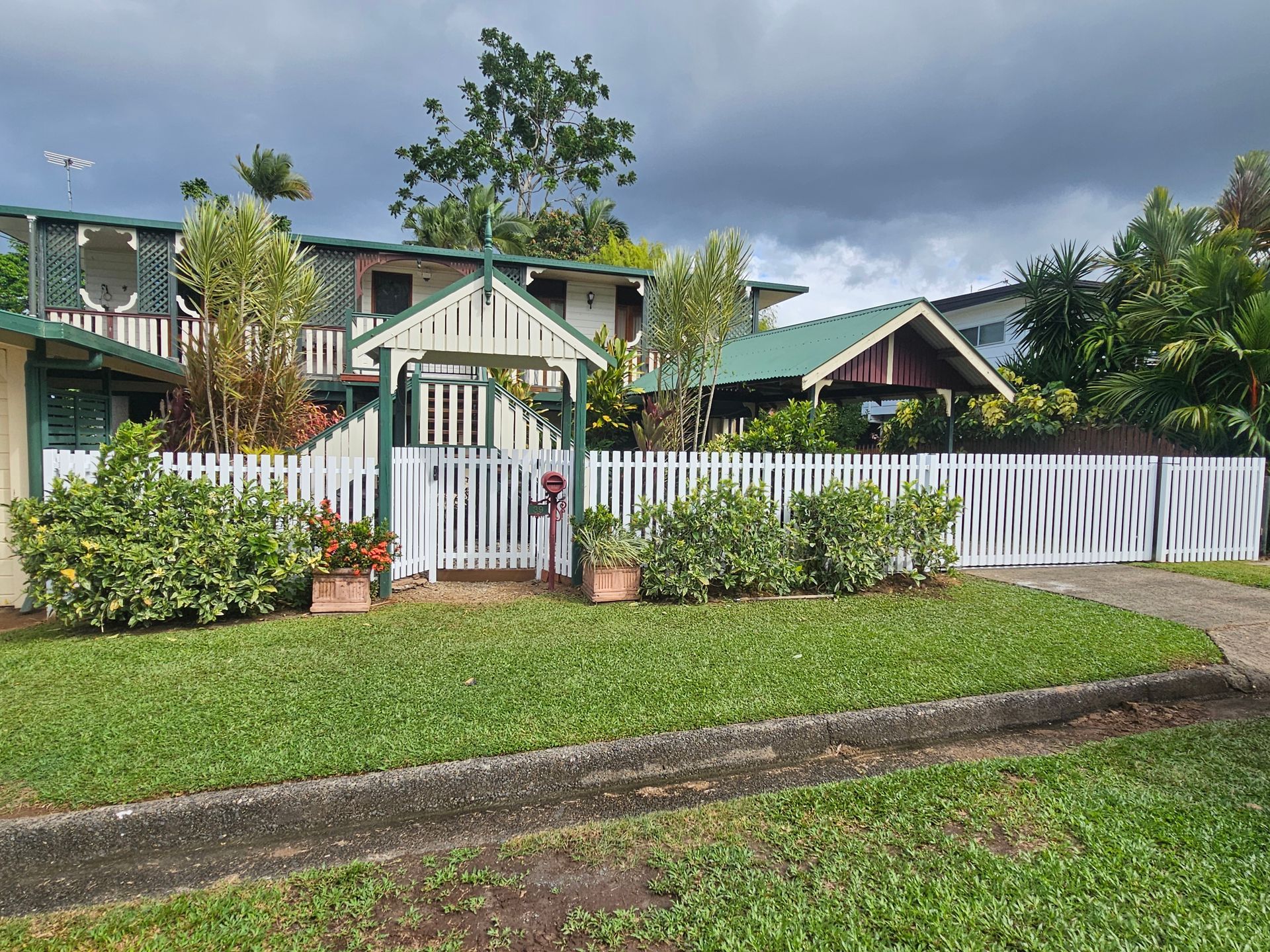 Small white house with green roof, front gate, and white picket fence under a cloudy sky. — KLS Fencing In Edmonton, QLD