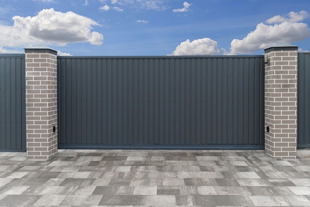 Gray metal sliding gate between brick pillars under a blue sky with clouds. — KLS Fencing In Edmonton, QLD