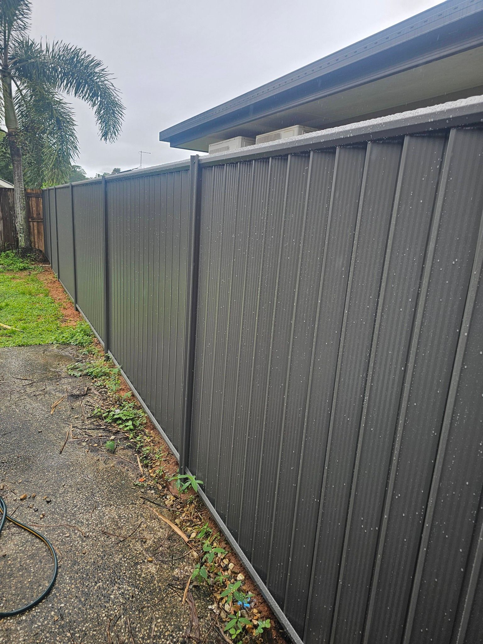Dark gray fence along a gravel path beside a house, with greenery on the left. — KLS Fencing In Tablelands, QLD