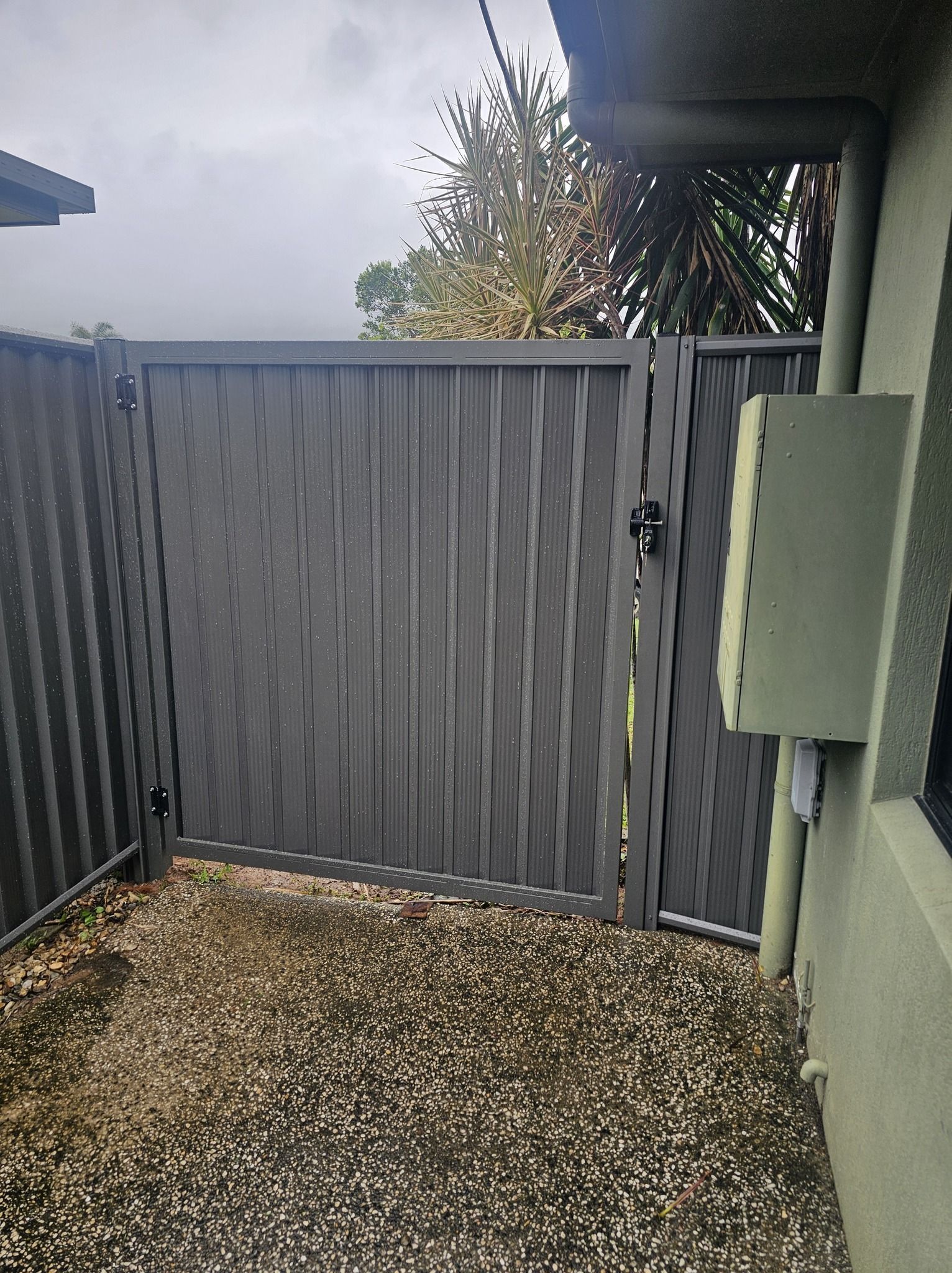 Narrow outdoor patio with gray gate, green walls, and gravel ground under an overcast sky. — KLS Fencing In Normanton, QLD