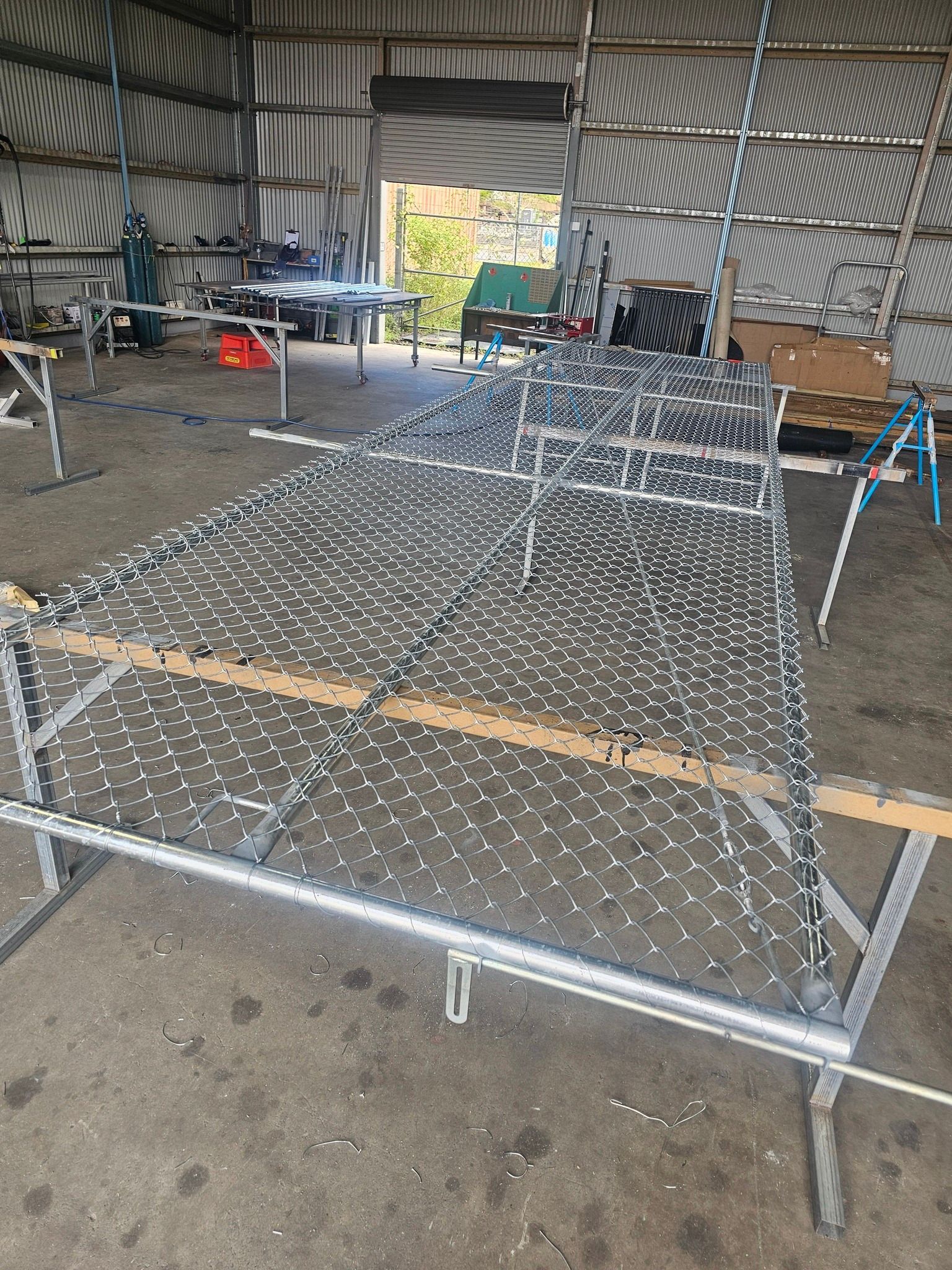 Large metal animal cage frame in a workshop with wire mesh partially attached — KLS Fencing In Edmonton, QLD