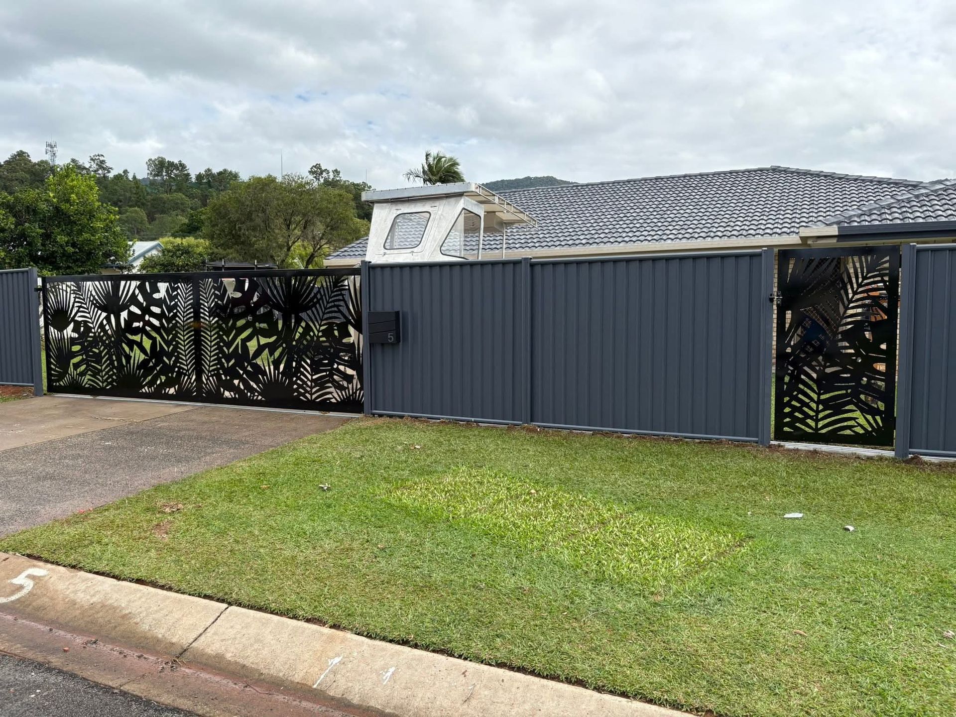 Single-story house with dark blue fence and gate, gray roof, and green lawn along a street.