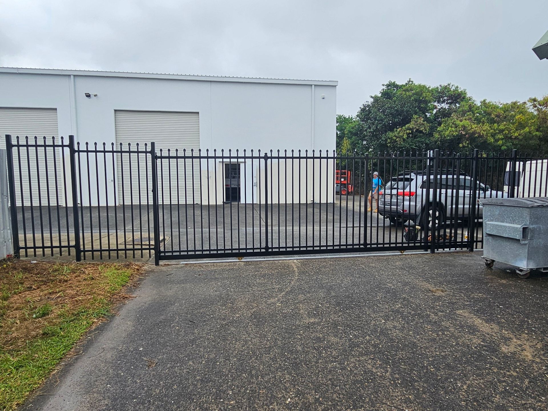 Closed black metal gate in front of a white building, with a car and trash bins nearby. — KLS Fencing In Innisfail, QLD