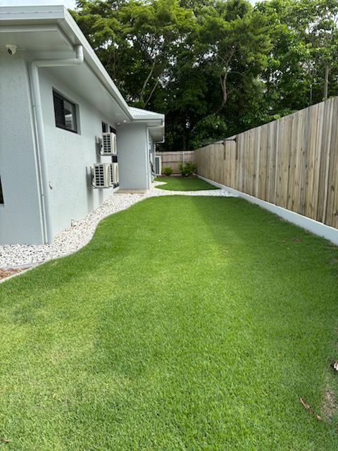 Narrow side yard with bright green grass, white house wall, and wooden fence along the right side