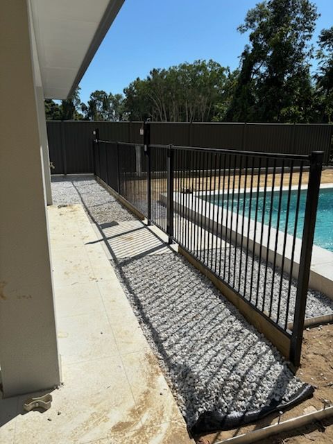 Black metal pool safety fence along a sunlit concrete patio beside a swimming pool.