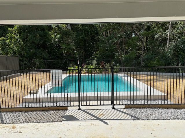Backyard pool with a black metal safety fence and gate in front of turquoise water