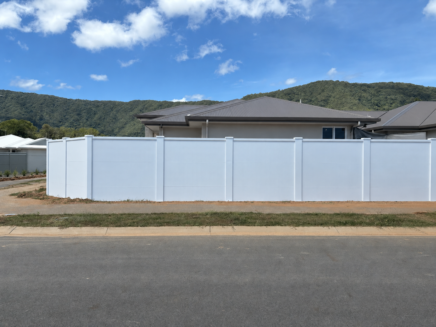 White privacy fence in front of a suburban house with mountains and blue sky behind it
