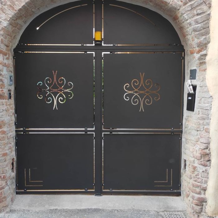 Cancello in metallo nero con dettagli decorativi dorati in un arco in mattoni.