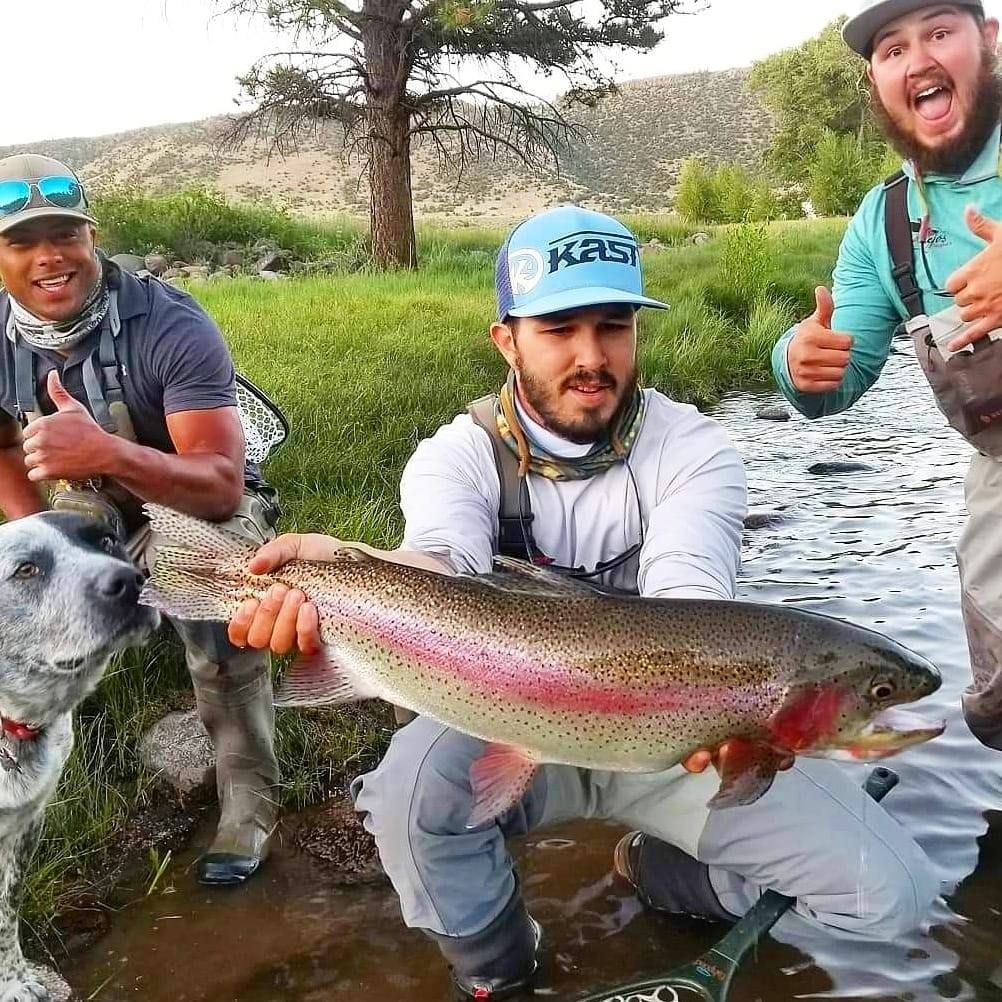 A man wearing a hat that says ' kraus ' on it is holding a large fish