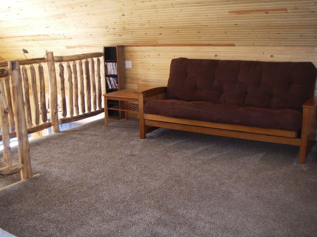 A living room with a brown futon and a wooden railing
