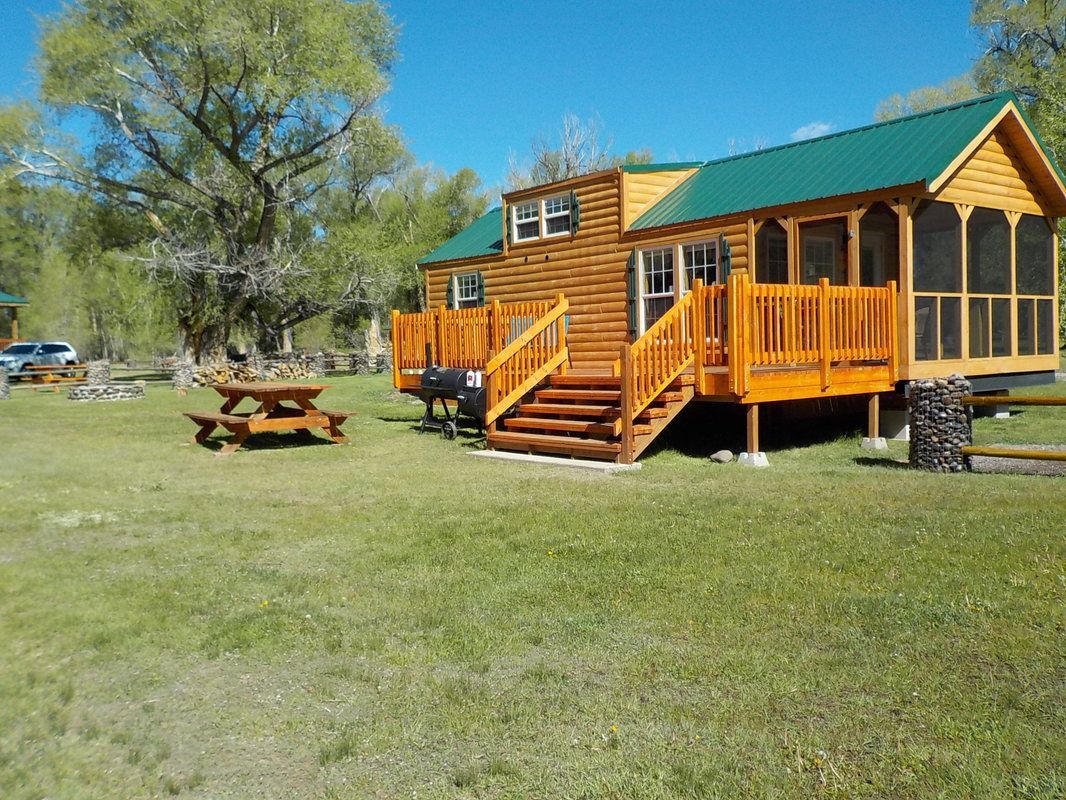 A log cabin with a screened in porch and a picnic table in front of it.