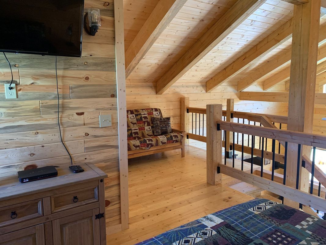 A living room in a log cabin with a futon and a flat screen tv.