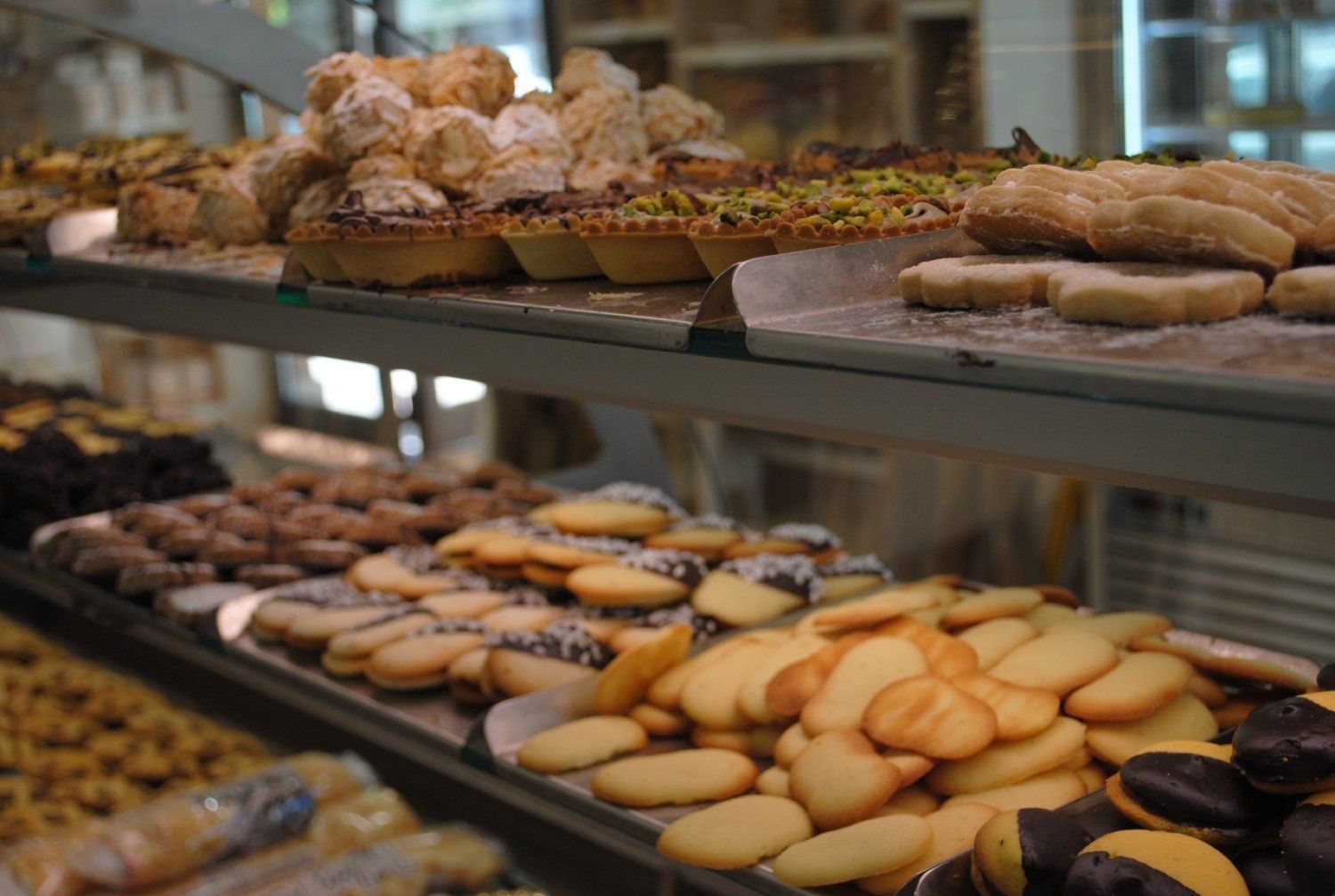 Assortimento di pasticcini e biscotti disposti su vassoi in una vetrina di una pasticceria.